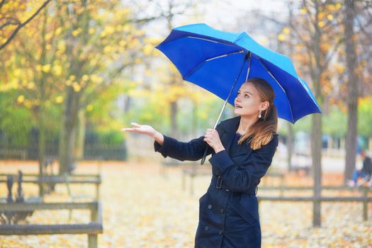 Beautiful young woman with blue umbrella in the Luxembourg garden of Paris on a fall or spring rainy day