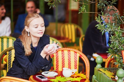 Beautiful young woman drinking hot chocolate in Parisian outdoor cafe on a nice fall day