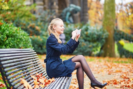 Beautiful young woman on a street of Paris on a sunny fall or spring day taking selfie with her mobile phone