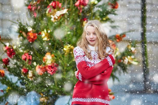Girl with a brightly decorated Christmas tree, under the falling snow