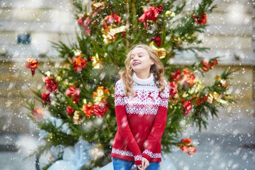Girl with a brightly decorated Christmas tree, under the falling snow