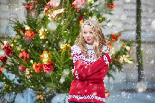 Girl with a brightly decorated Christmas tree in Paris during snowfall