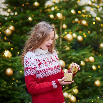 Cheerful girl with Christmas present near decorated Christmas tree