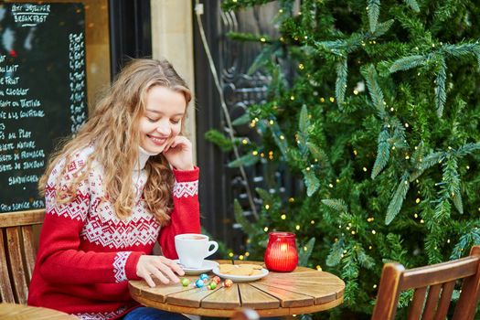 Beautiful young girl in an outdoor Parisian cafe on a winter day, drinking hot chocolate