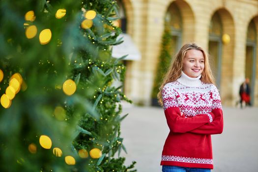 Cheerful young woman on a street of Paris decorated for Christmas