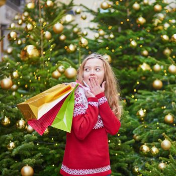 Cheerful young girl with colorful shopping bags near Christmas tree