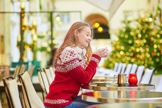 Beautiful young girl in an outdoor Parisian cafe on a winter day, drinking hot chocolate