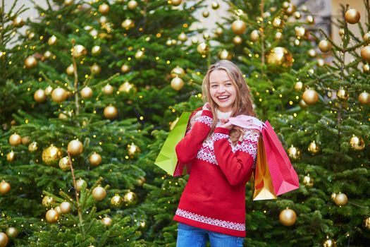 Cheerful young woman on a street of Paris decorated for Christmas with shopping bags