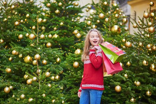Cheerful young woman on a street of Paris decorated for Christmas with shopping bags