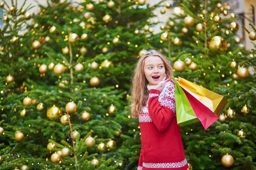 Cheerful young woman on a street of Paris decorated for Christmas with shopping bags