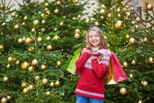 Cheerful young girl with colorful shopping bags near Christmas tree