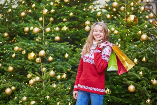 Cheerful young woman on a street of Paris decorated for Christmas with shopping bags