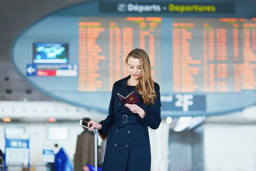 Young woman in international airport near the flight information board, looking in her passport