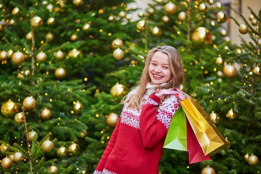 Cheerful young girl with colorful shopping bags near Christmas tree