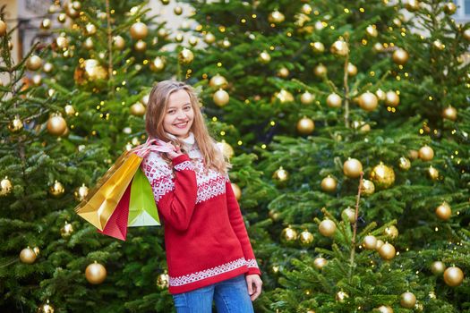 Cheerful young girl with colorful shopping bags near Christmas tree
