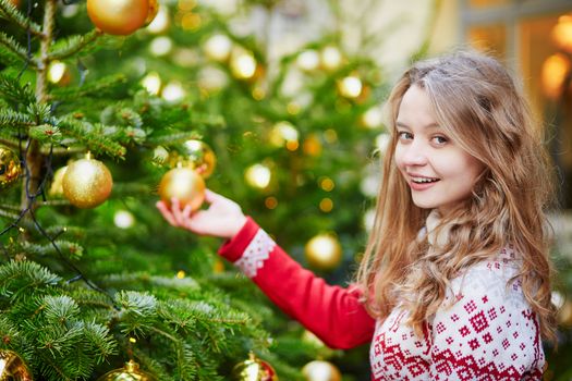 Girl decorating Christmas tree with golden balls