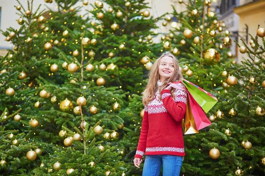 Cheerful young woman on a street of Paris decorated for Christmas with shopping bags