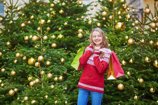 Cheerful young woman on a street of Paris decorated for Christmas with shopping bags