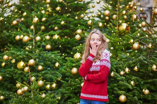 Cheerful young woman on a street of Paris decorated for Christmas with shopping bags
