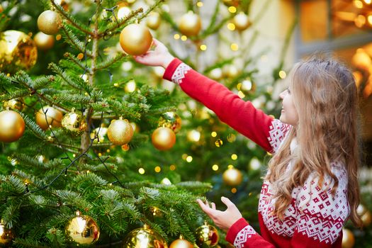 Cheerful young woman decorating Christmas tree with golden balls