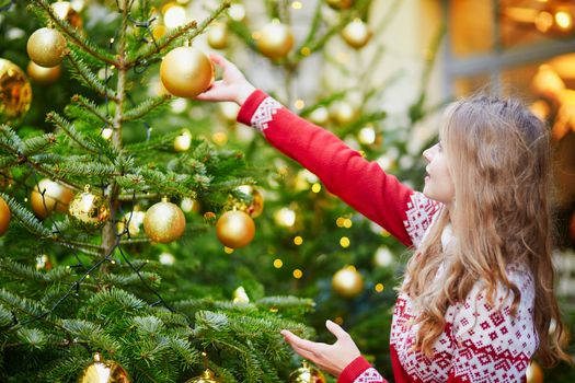 Girl decorating Christmas tree with golden balls