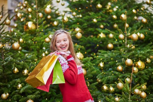 Cheerful young girl with colorful shopping bags near Christmas tree