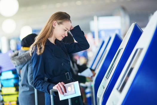 Young woman in international airport doing self check-in, stressed and concerned. Missed, delayed or canceled flight concept