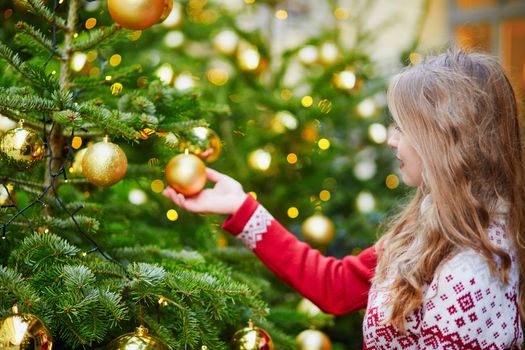 Cheerful young woman decorating Christmas tree with golden balls