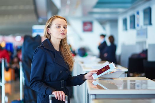 Young woman in international airport at check-in counter, giving her passport to an officer and waiting for her boarding pass