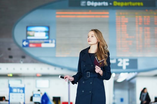 Young woman in international airport near the flight information board, holding French passport in her hand