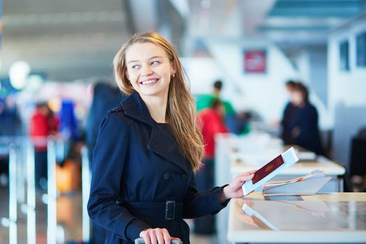 Young woman in international airport at check-in counter, giving her passport to an officer and waiting for her boarding pass