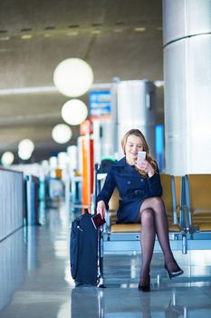 Young woman in international airport, waiting for her flight, using her mobile phone