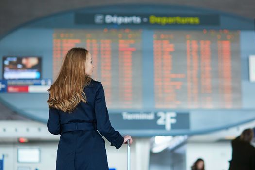 Young woman in international airport looking at the flight information board, checking her flight