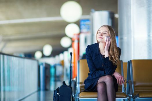 Young woman in international airport, waiting for her flight, using her mobile phone