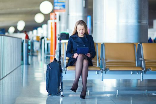 Young woman in international airport, waiting for her flight, using her tablet