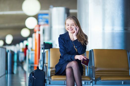 Young woman in international airport, waiting for her flight, using her mobile phone