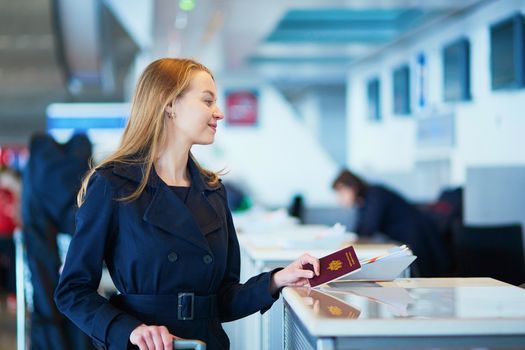 Young woman in international airport at check-in counter, giving her passport to an officer and waiting for her boarding pass