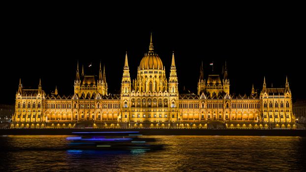 Long exposure image of the illuminated Hungarian Parliament in Budapest at night with a cruise vessel in front.