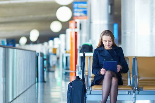 Young woman in international airport, waiting for her flight, using her tablet