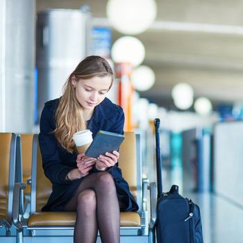 Young woman in international airport reading a book while waiting for her flight