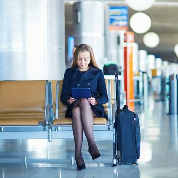 Young woman in international airport reading a book on tablet while waiting for her flight