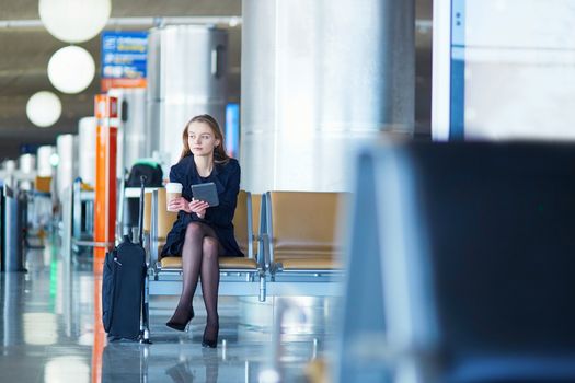 Young woman in international airport, reading and drinking coffee while waiting for her flight