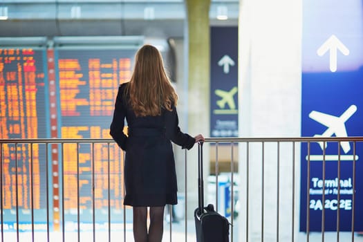 Young woman in international airport looking at the flight information board, checking her flight