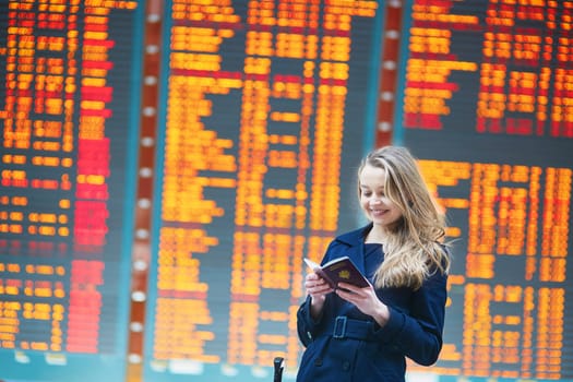 Young woman in international airport near the flight information board, checking her passport