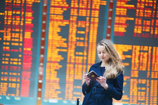 Young woman in international airport near the flight information board, checking her passport