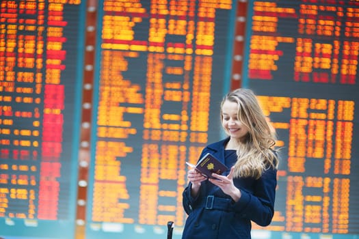 Young woman in international airport near the flight information board, checking her passport