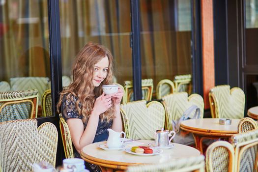 Beautiful Parisian woman in cafe, drinking coffee and eating macaroons, traditional French dessert