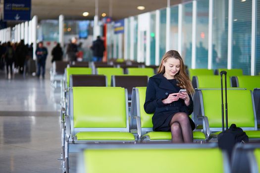 Young woman in international airport, checking her phone while waiting for her flight