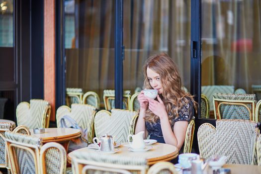 Beautiful Parisian woman in cafe, drinking coffee and eating macaroons, traditional French dessert