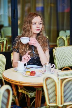 Beautiful Parisian woman in cafe, drinking coffee and eating macaroons, traditional French dessert